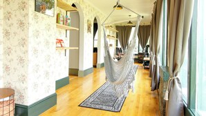 Una habitación con papel tapiz floral, una hamaca y vistas a un jardín a través de ventanas amplias.