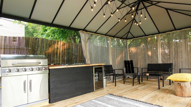 Un área de cocina exterior techada con una parrilla, barra y asientos.