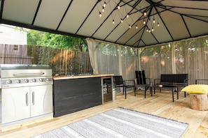 Un área de cocina exterior techada con una parrilla, barra y asientos.