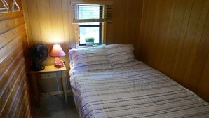 A small, cozy room with a bed, a desk with a lamp, and a window with blinds.