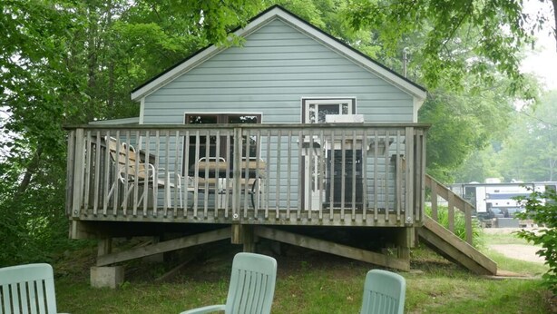 A small cabin with a deck, two chairs, and a staircase leading up to the entrance.