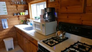 A wooden cabin kitchen with a gas stove, a coffee maker, a microwave, and a sink.