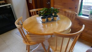 A wooden dining table with four chairs, a potted plant arrangement, and a window with a view of the outside.