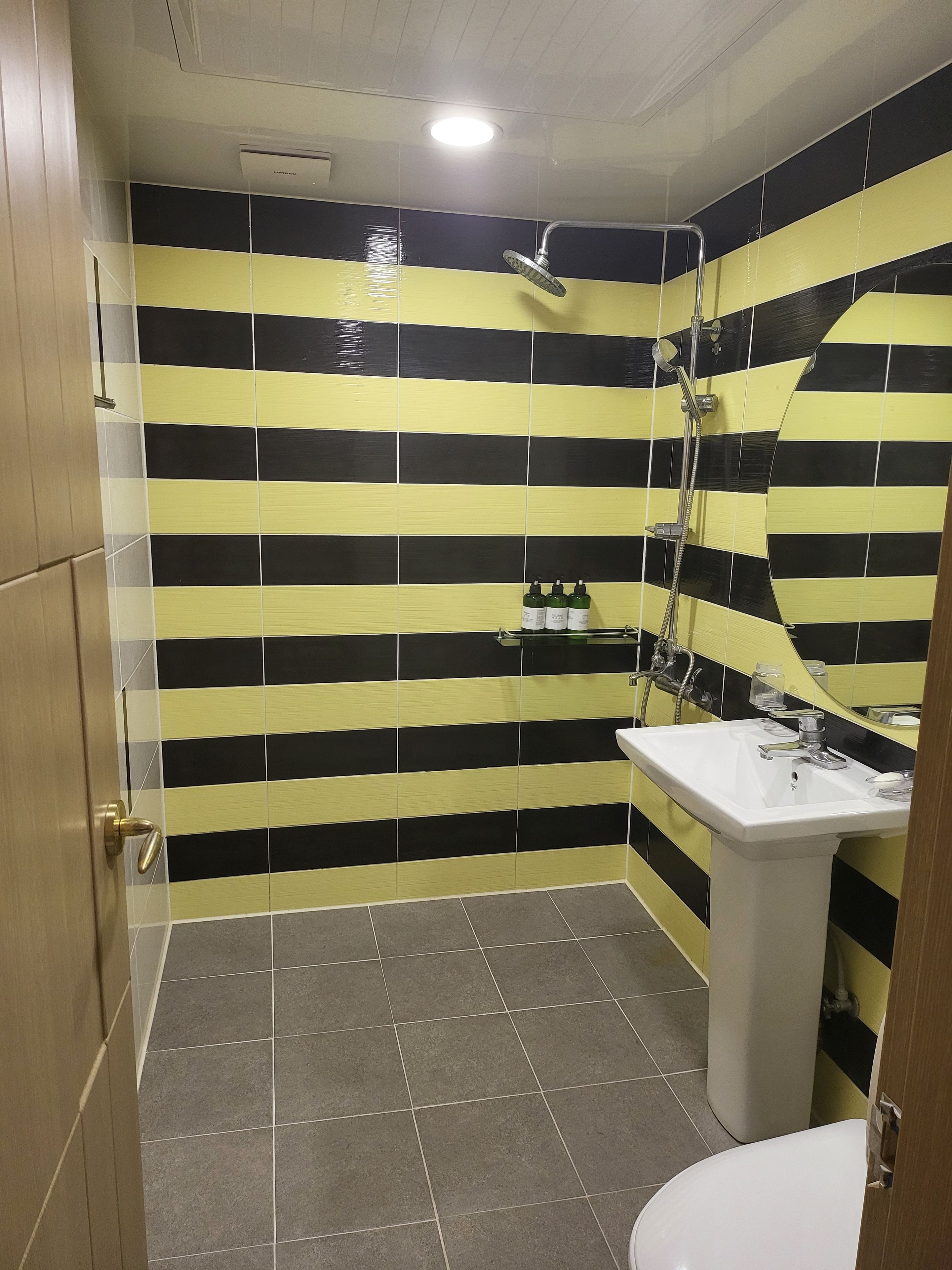 Casa de banho com parede de azulejos listrados, lavatório assentado, chuveiro e sanita.