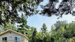 A two-story house with a balcony, surrounded by a grassy yard and dense trees. - Beautiful and private lakefront home on the sandy shores of South Twin Lake (Indian Purchase Township)