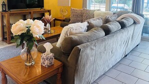 A living room with a sofa, a TV, a lamp, and a vase with flowers. - Beautiful and private lakefront home on the sandy shores of South Twin Lake (Indian Purchase Township)