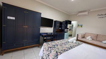 A hotel room with a large wardrobe, a desk with a chair, a bed with a floral bedspread, and a sofa with towels.