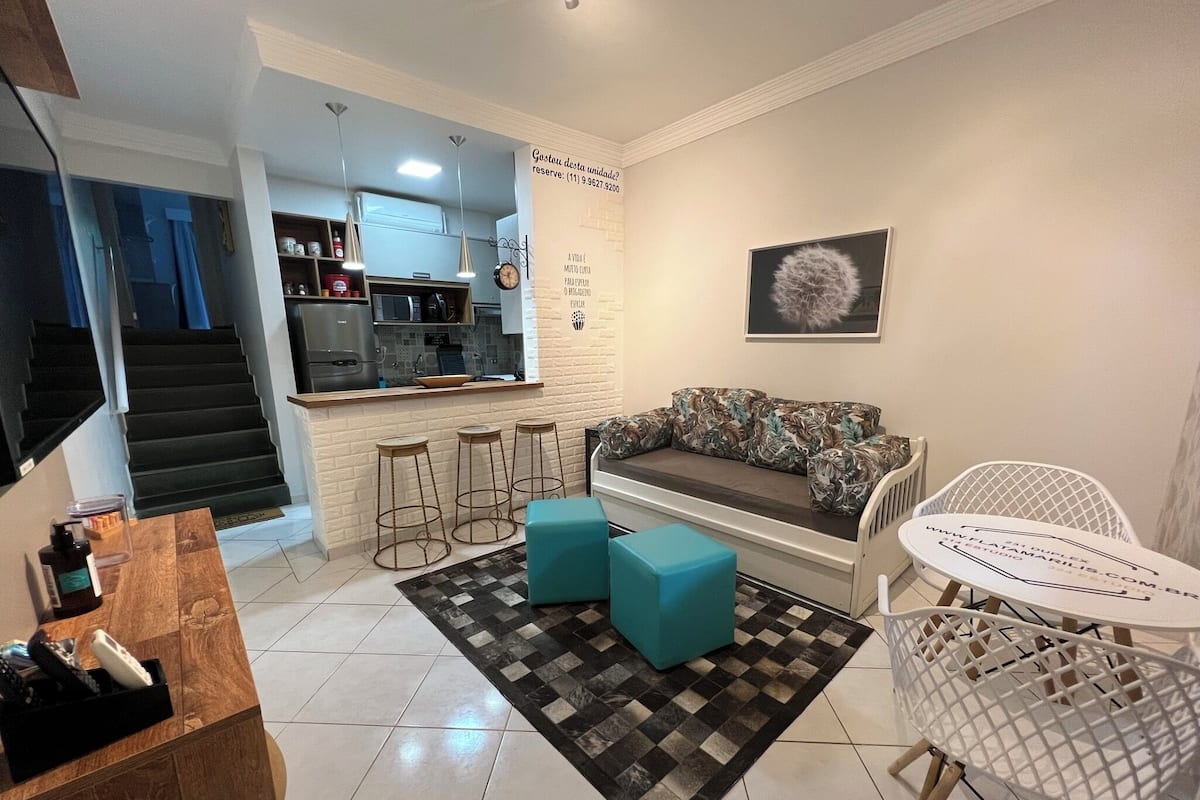 A modern living room with a sofa, two ottomans, a coffee table, and a dining area with a chair and a small table.