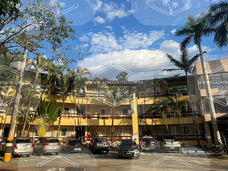 Un estacionamiento con varios coches aparcados frente a un edificio amarillo con múltiples ventanas y balcones.