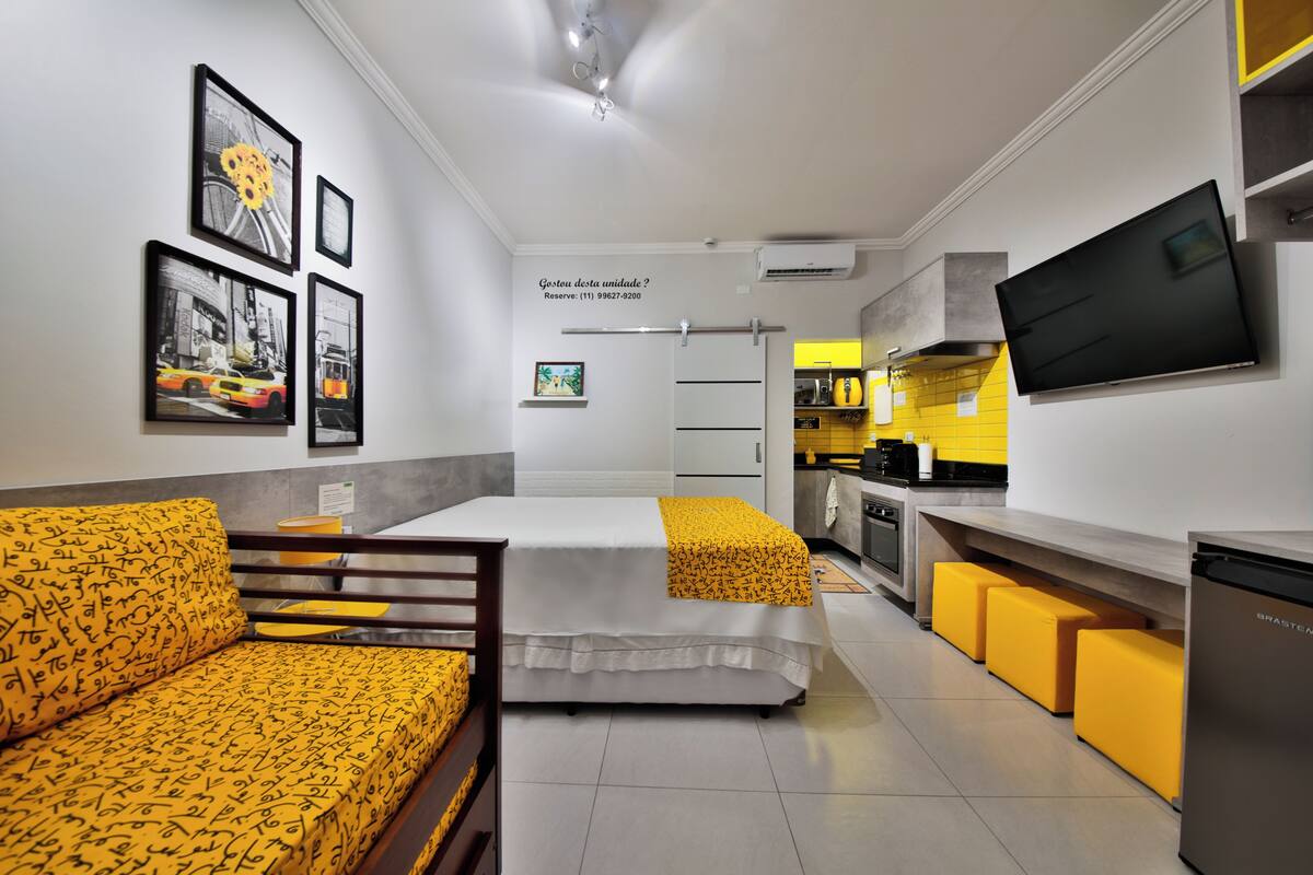 A compact hotel room with a bed, a sofa, a TV, and a kitchenette.
