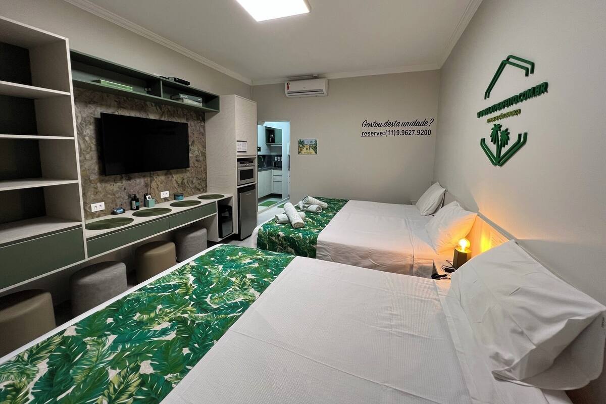A hotel room with two beds, a TV, a desk with a mirror, and a kitchenette.