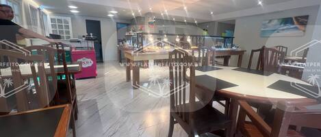 A dining area with wooden tables and chairs, a kitchen in the background, and a counter with a pink machine.