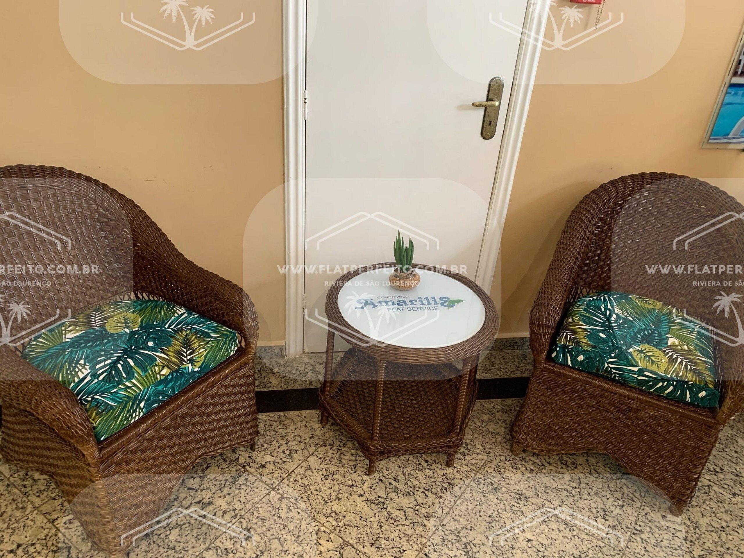 Two wicker chairs with tropical leaf-patterned cushions, a small round table with a decorative item, and a white door in the background.