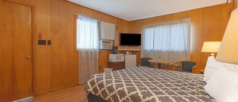 Une chambre d’hôtel avec un grand lit, un bureau avec une télévision, un four à micro-ondes et une petite table avec une chaise.