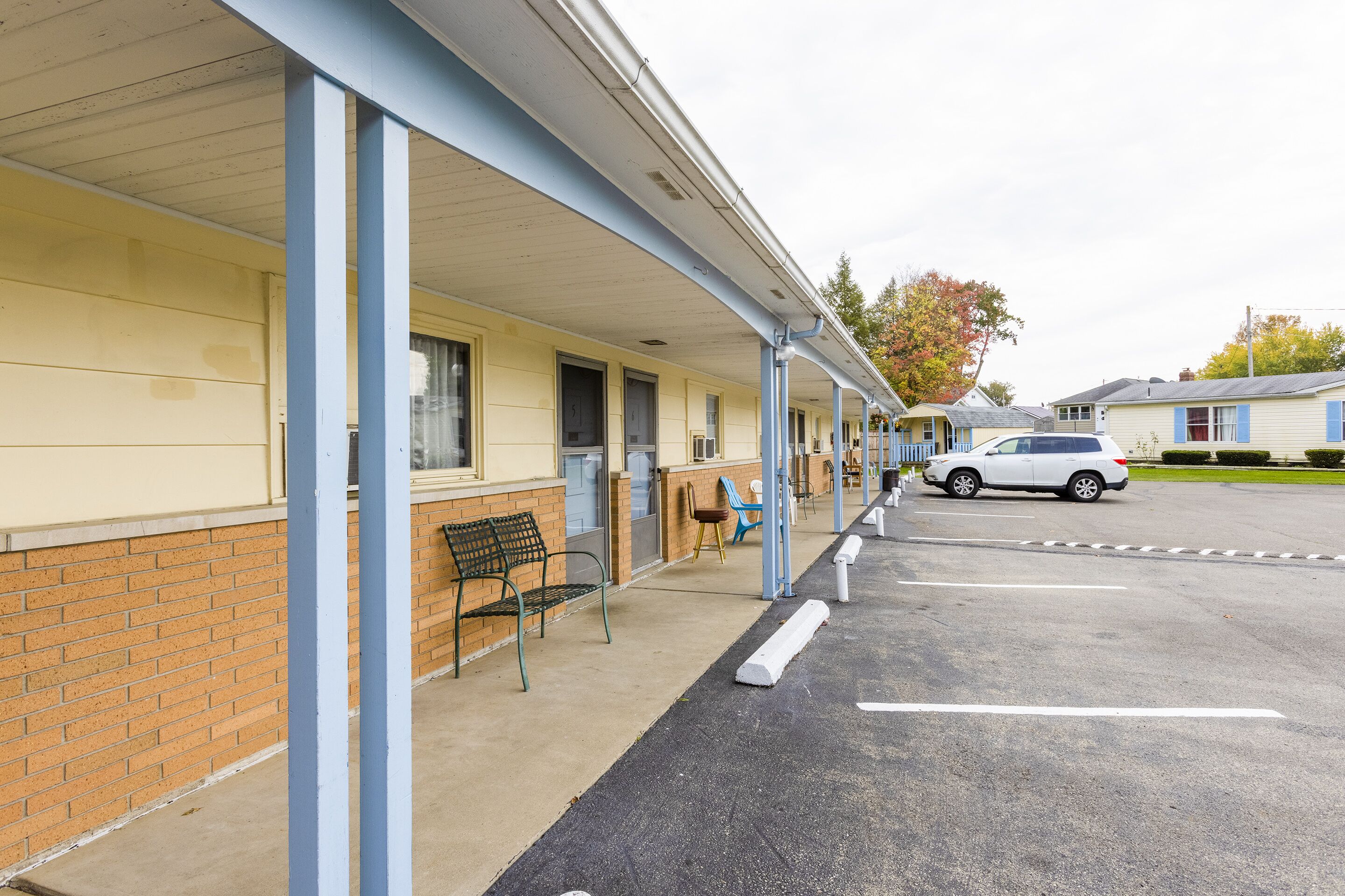 Un motel doté d’un parking couvert, d’une rangée de chambres aux fenêtres encadrées de bleu et d’une voiture garée.