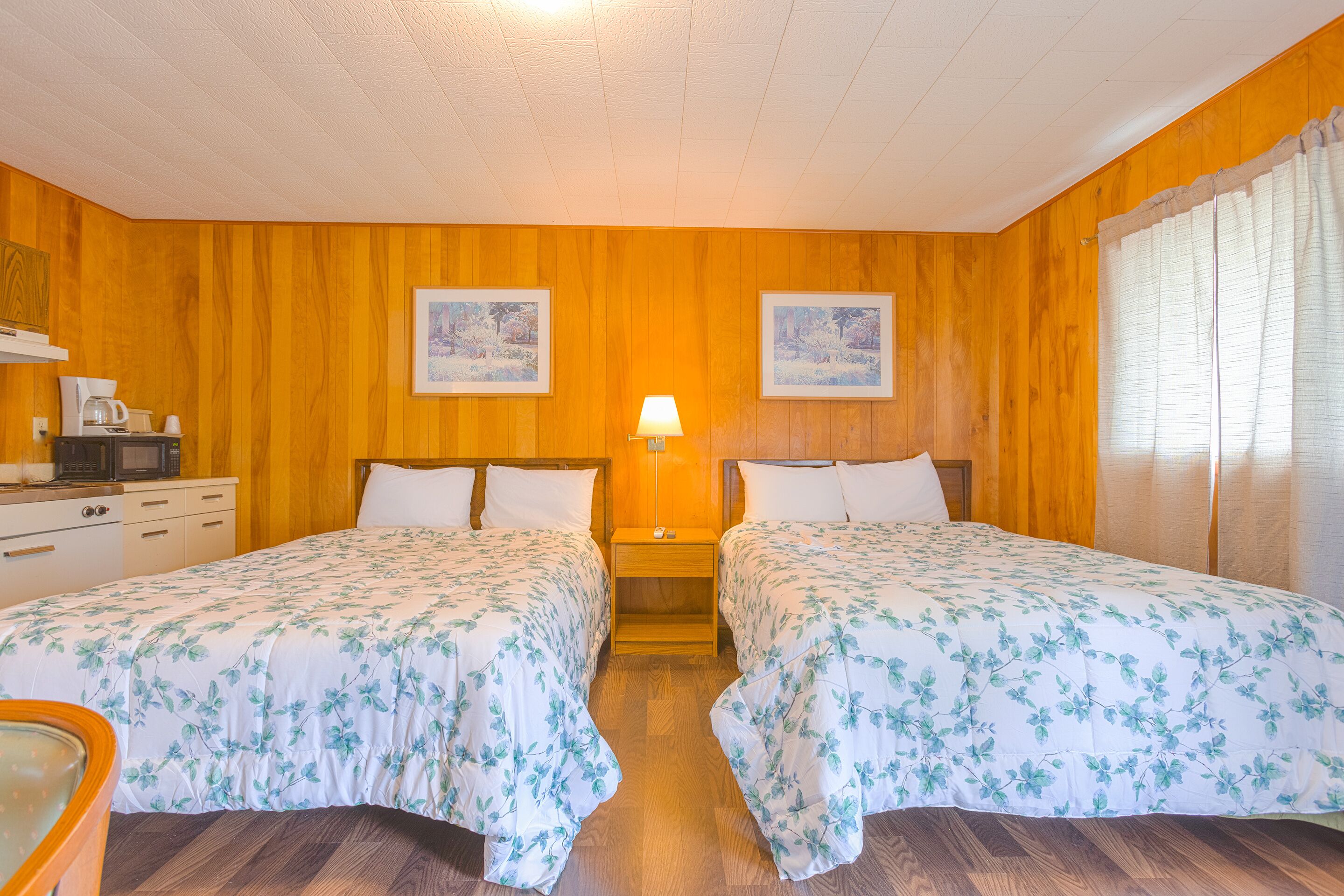 A room with two beds, wooden walls, a coffee maker, and framed pictures on the wall.