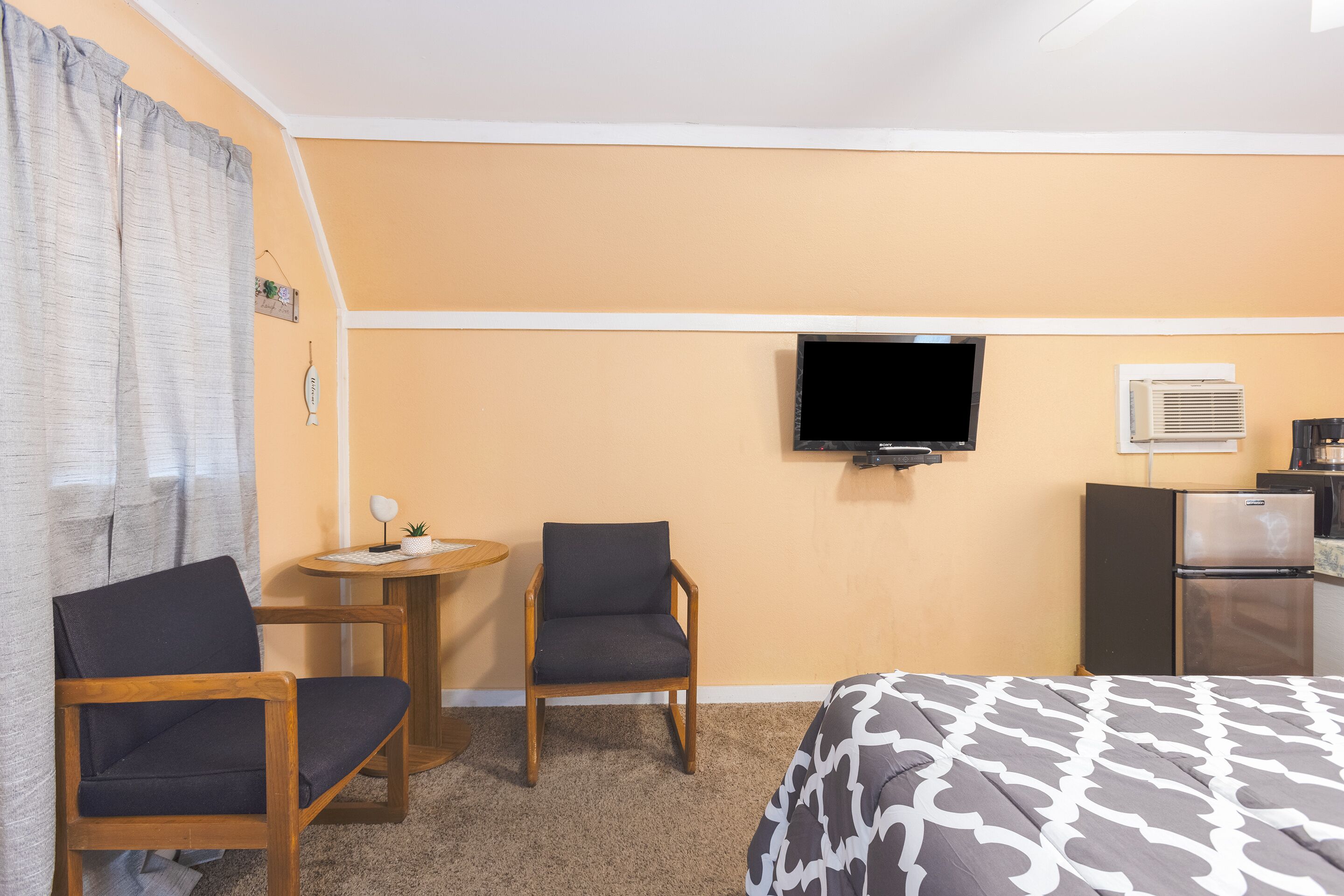 A hotel room with a bed, two chairs, a small table, a television, and a refrigerator.