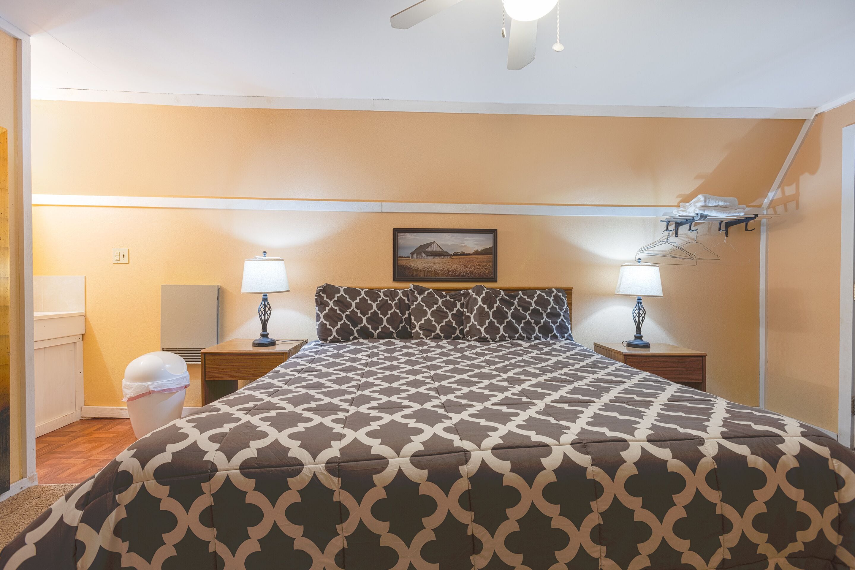 A neatly made bed with a patterned bedspread, two bedside tables with lamps, a picture on the wall, and a ceiling fan.