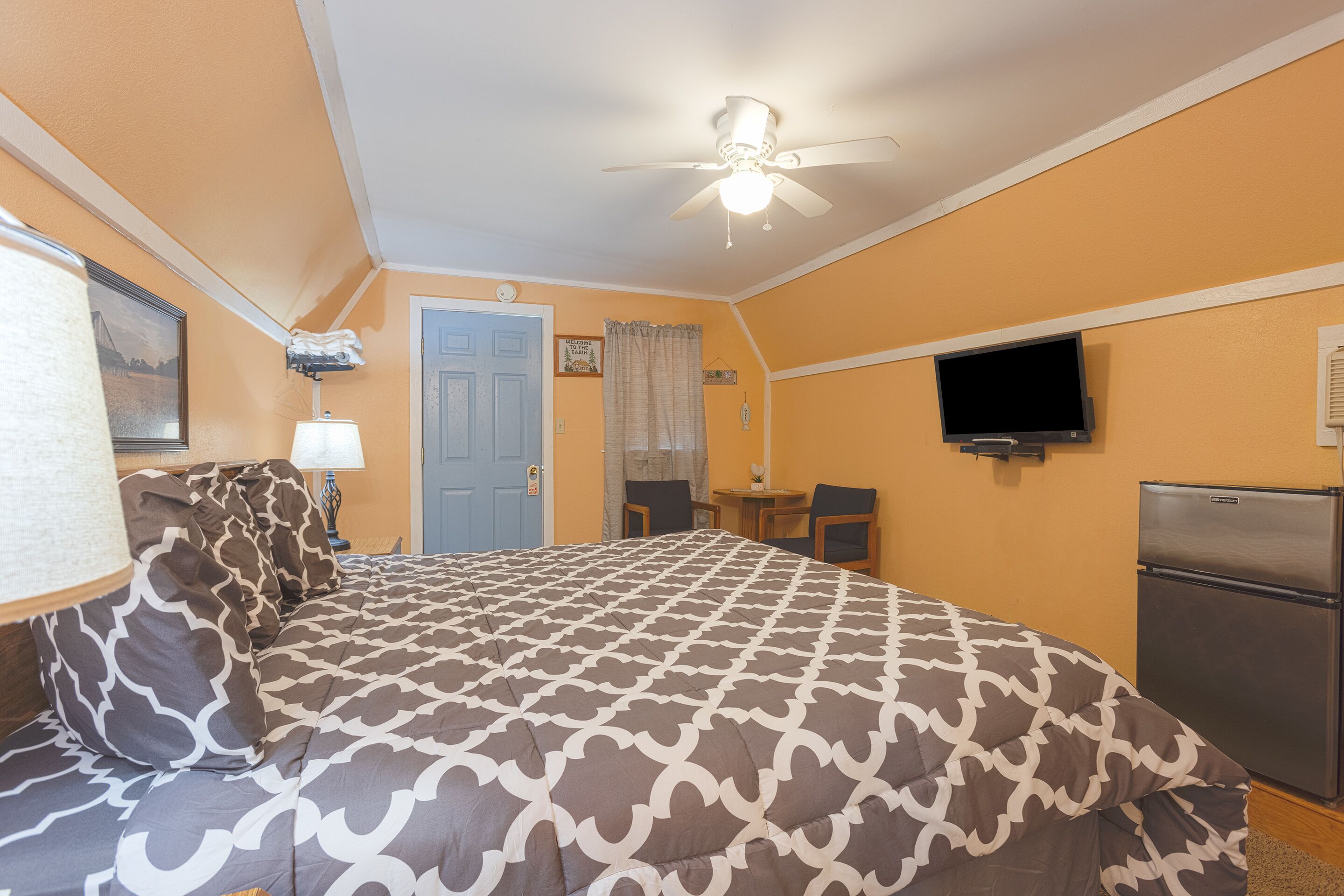 A bedroom with a bed, a ceiling fan, a television, and a refrigerator.
