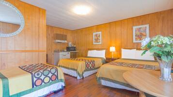 A hotel room with two beds, a wooden floor, a mirror, a desk, a lamp, and a vase with flowers.
