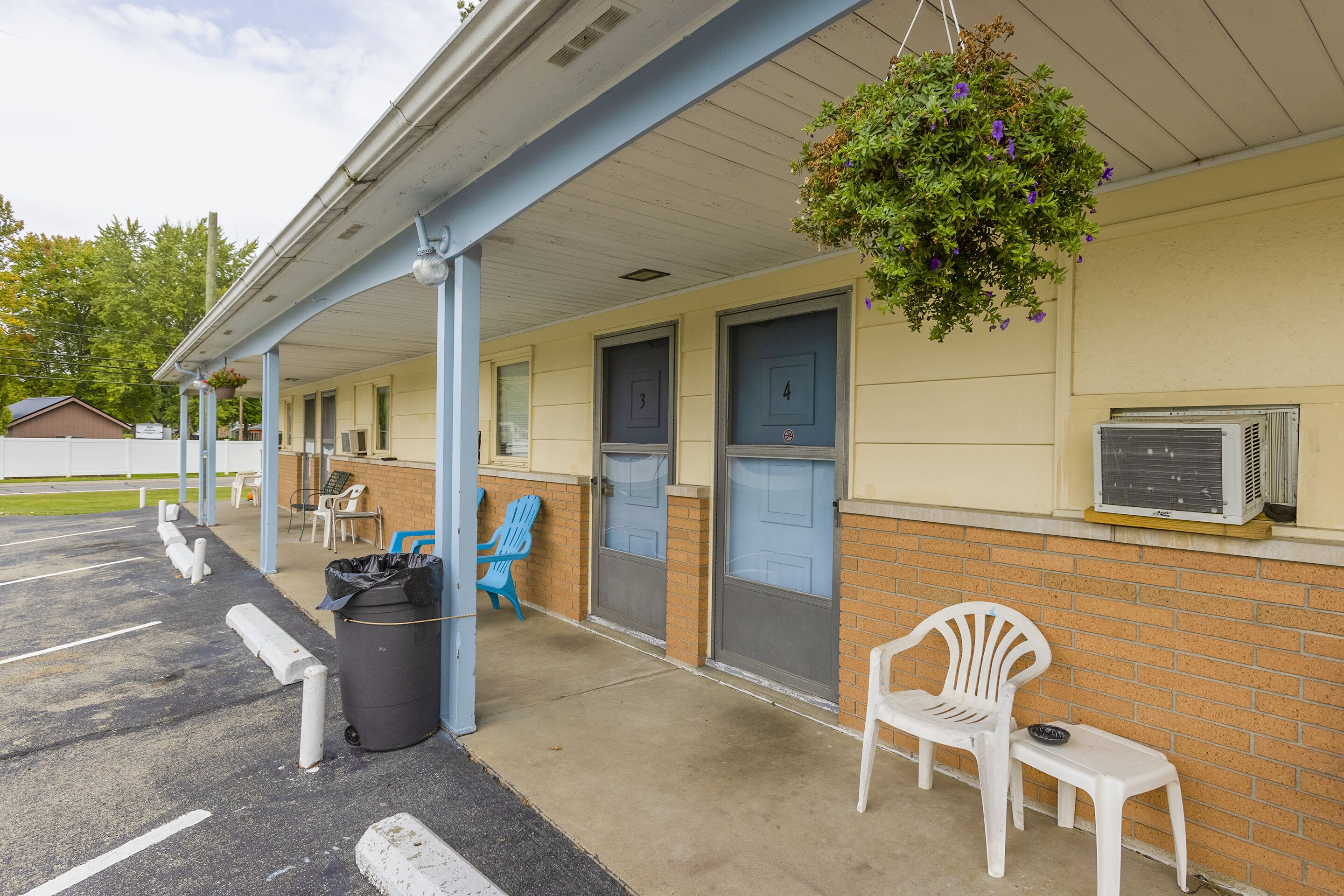 Un motel doté d’un parking couvert, de chambres numérotées et d’un espace extérieur aménagé avec des sièges.