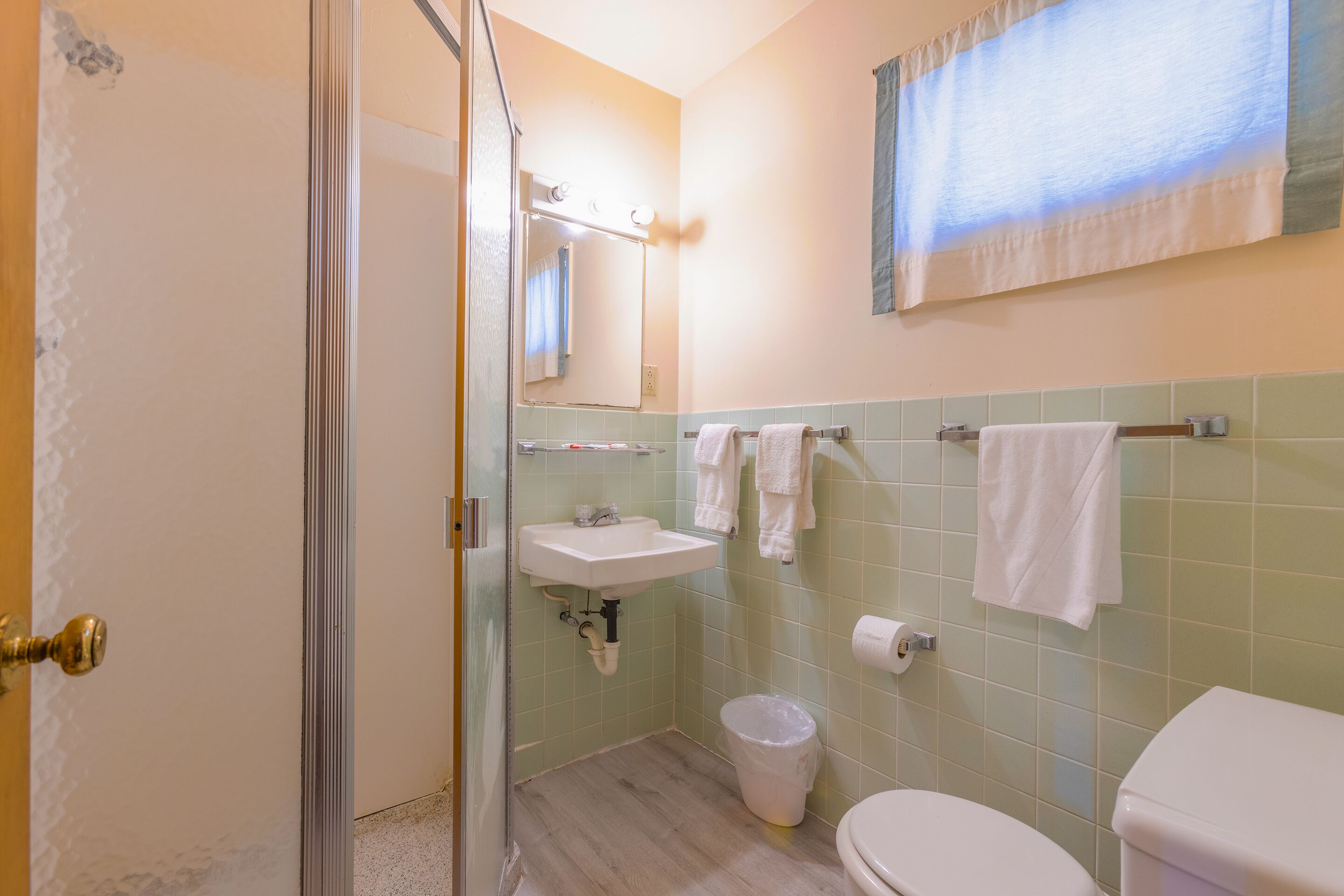 Un baño con lavamanos, espejo, toallero, inodoro y un cesto de basura.