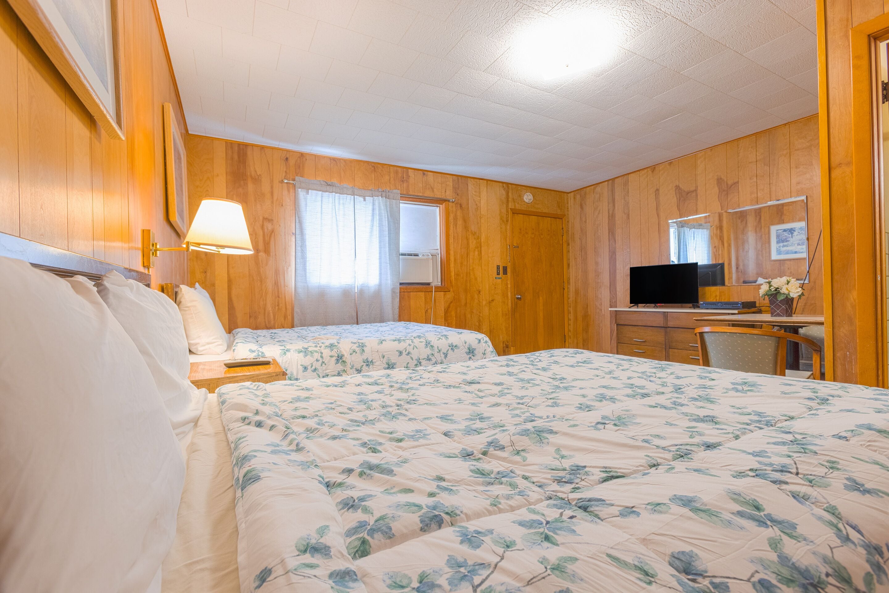A room with two beds, a desk, a chair, a television, and a mirror.