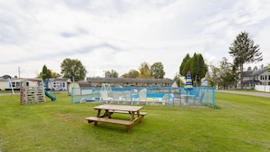 Una mesa de picnic en un área verde con una piscina rodeada por una cerca y un motel al fondo.