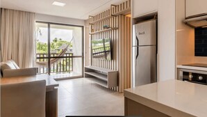 A modern kitchen with a built-in refrigerator, a dining area with a sofa, and a TV mounted on a wooden panel. - BCMA (Ipojuca)