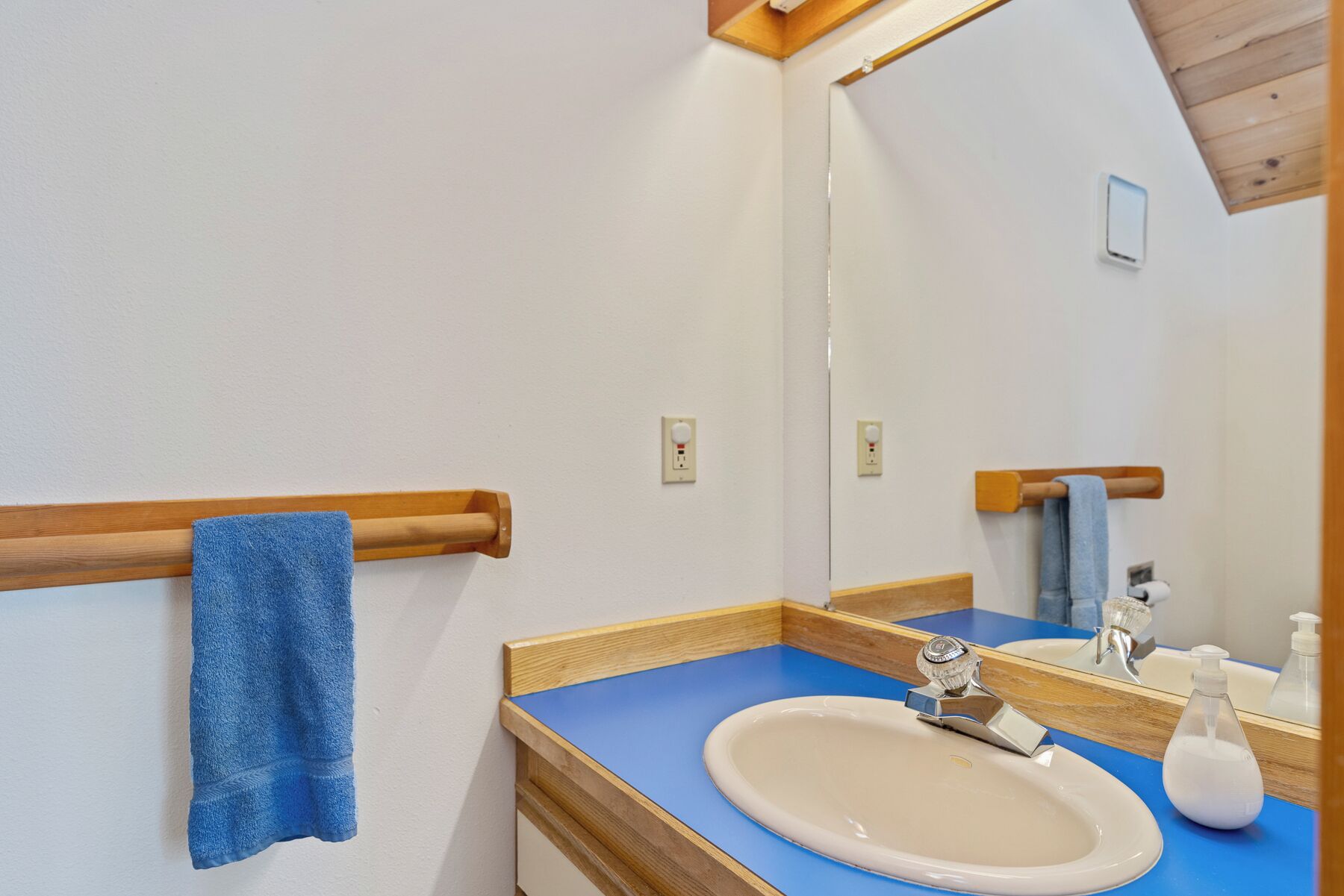 A bathroom with a wooden towel rack, a sink, a mirror, and a blue countertop.