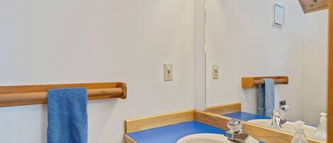 A bathroom with a wooden towel rack, a sink, a mirror, and a blue countertop.