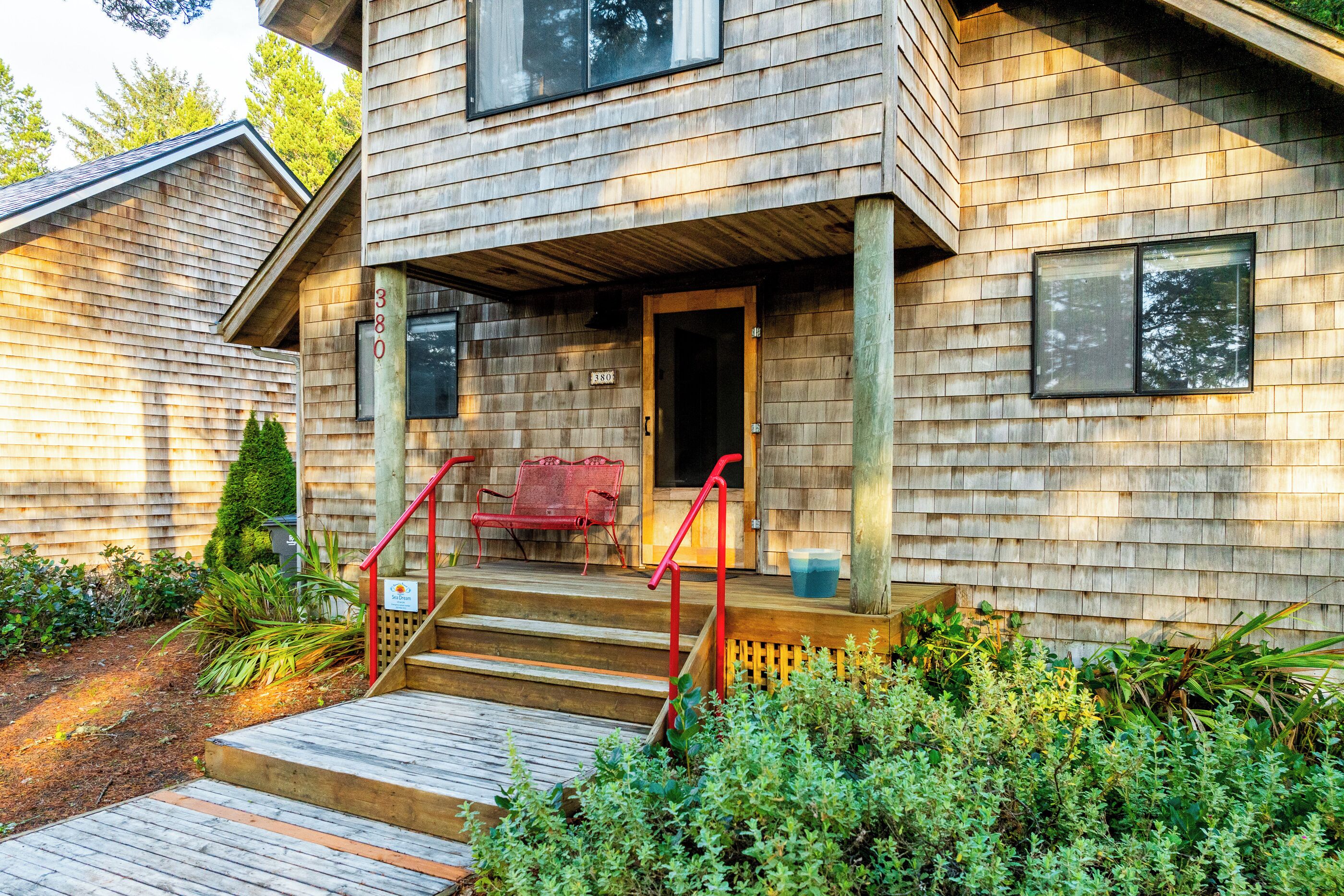 A wooden house with a porch, steps, and a red chair.