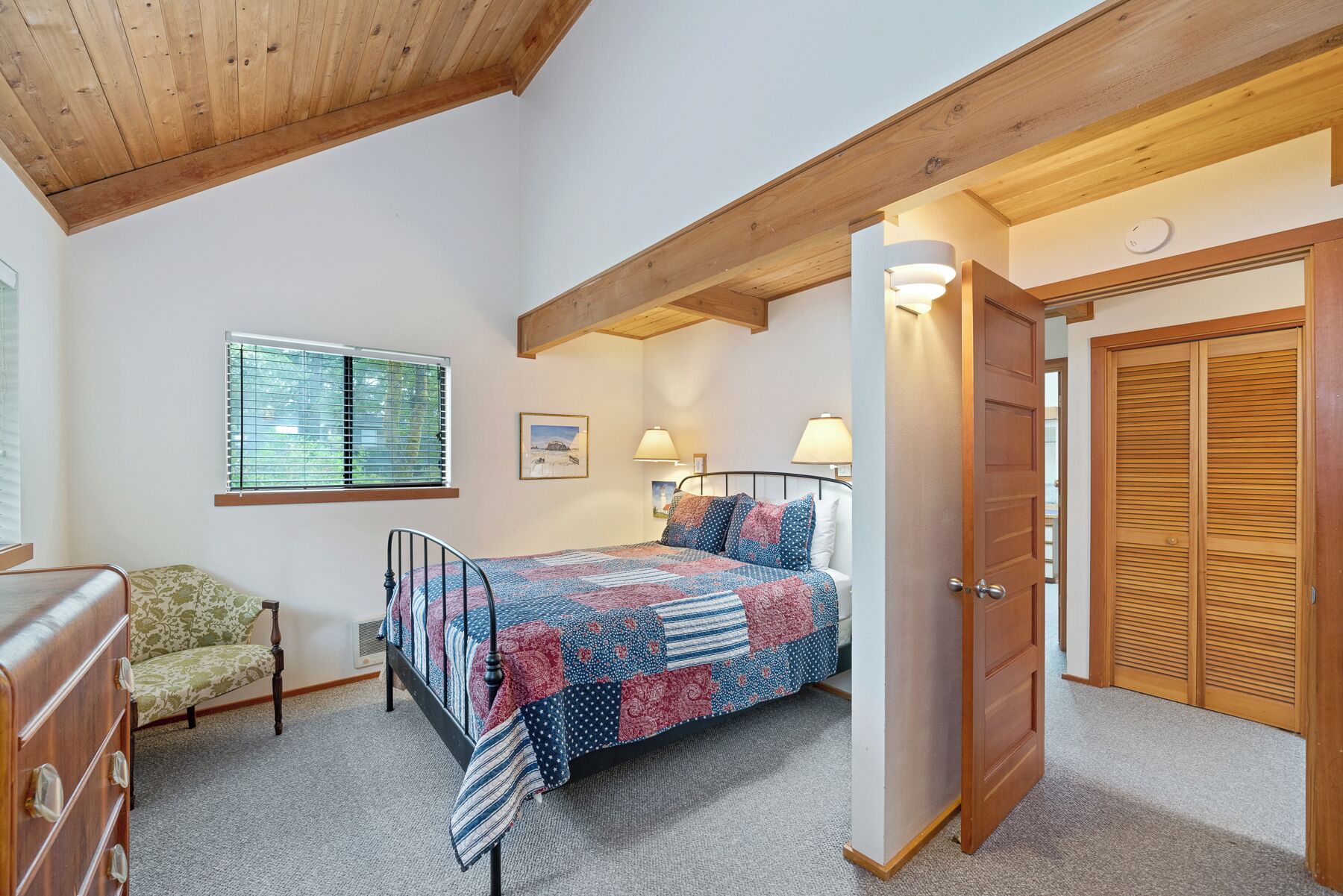 A bedroom with a bed, a chair, a dresser, a window, and a door.