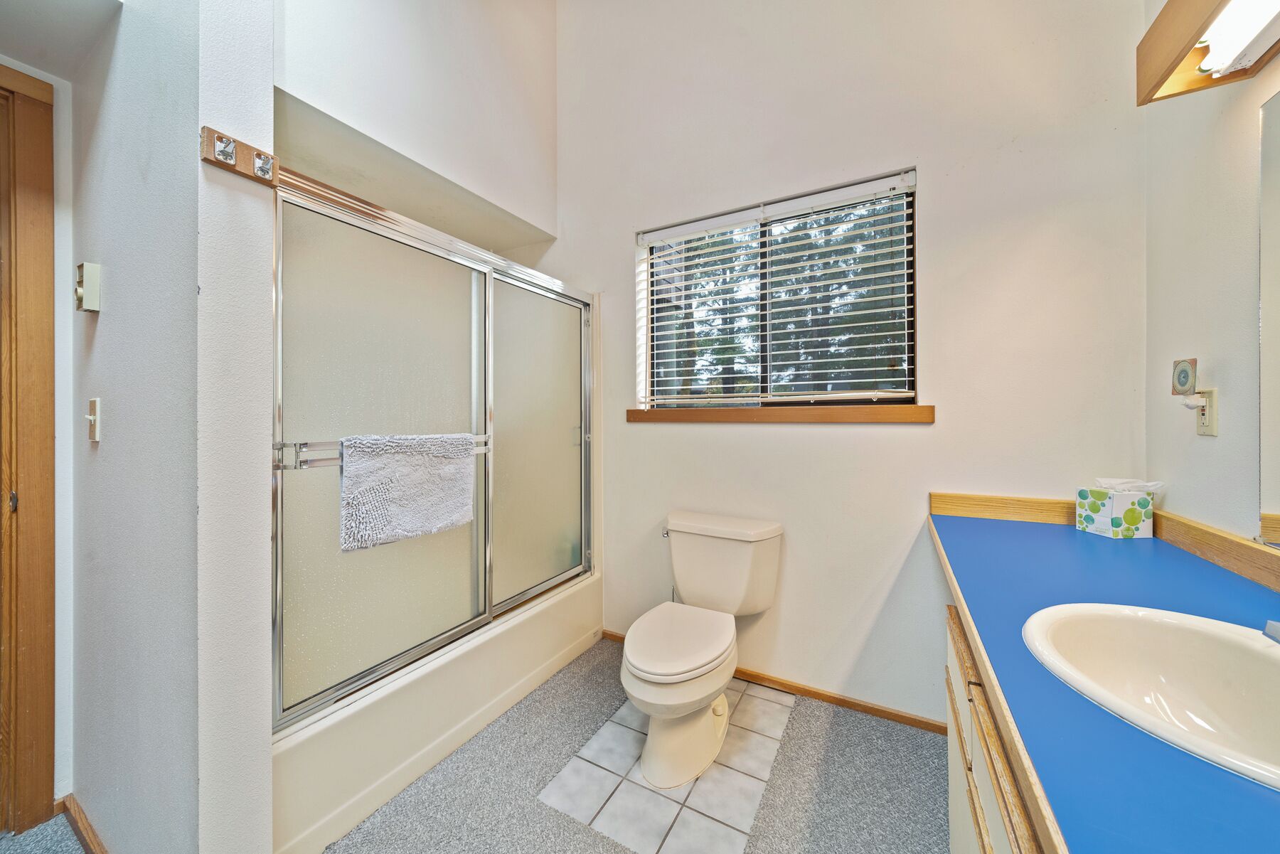 A bathroom with a shower, toilet, sink, and window.