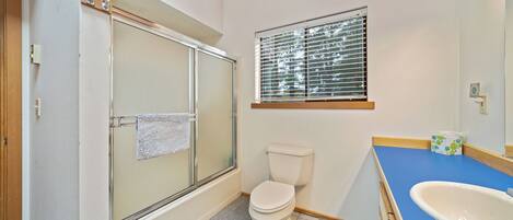 A bathroom with a shower, toilet, sink, and window.