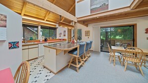 Una cocina amplia con una isla central, comedor de madera y grandes ventanales con vistas al exterior.