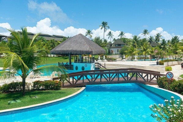 A swimming pool with a thatched-roof gazebo, palm trees, and a bridge. - BCMA Muro Alto (Ipojuca)