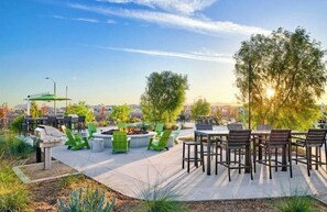 Relax in the outdoor patio area with comfortable seating, a dining table, and a grill, surrounded by lush landscaping and city views.