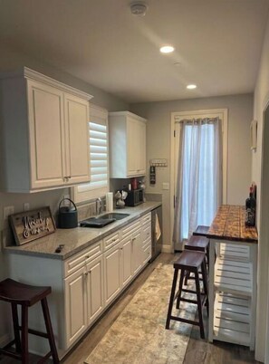 Compact kitchen with sink, microwave, and kettle, featuring a window with a curtain.