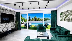 Una sala de estar moderna con televisor, sofás verdes, una piscina y un ventanal grande.