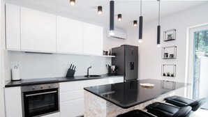 Una cocina moderna con armarios blancos, encimera negra, horno empotrado y una isla negra con taburetes de bar.