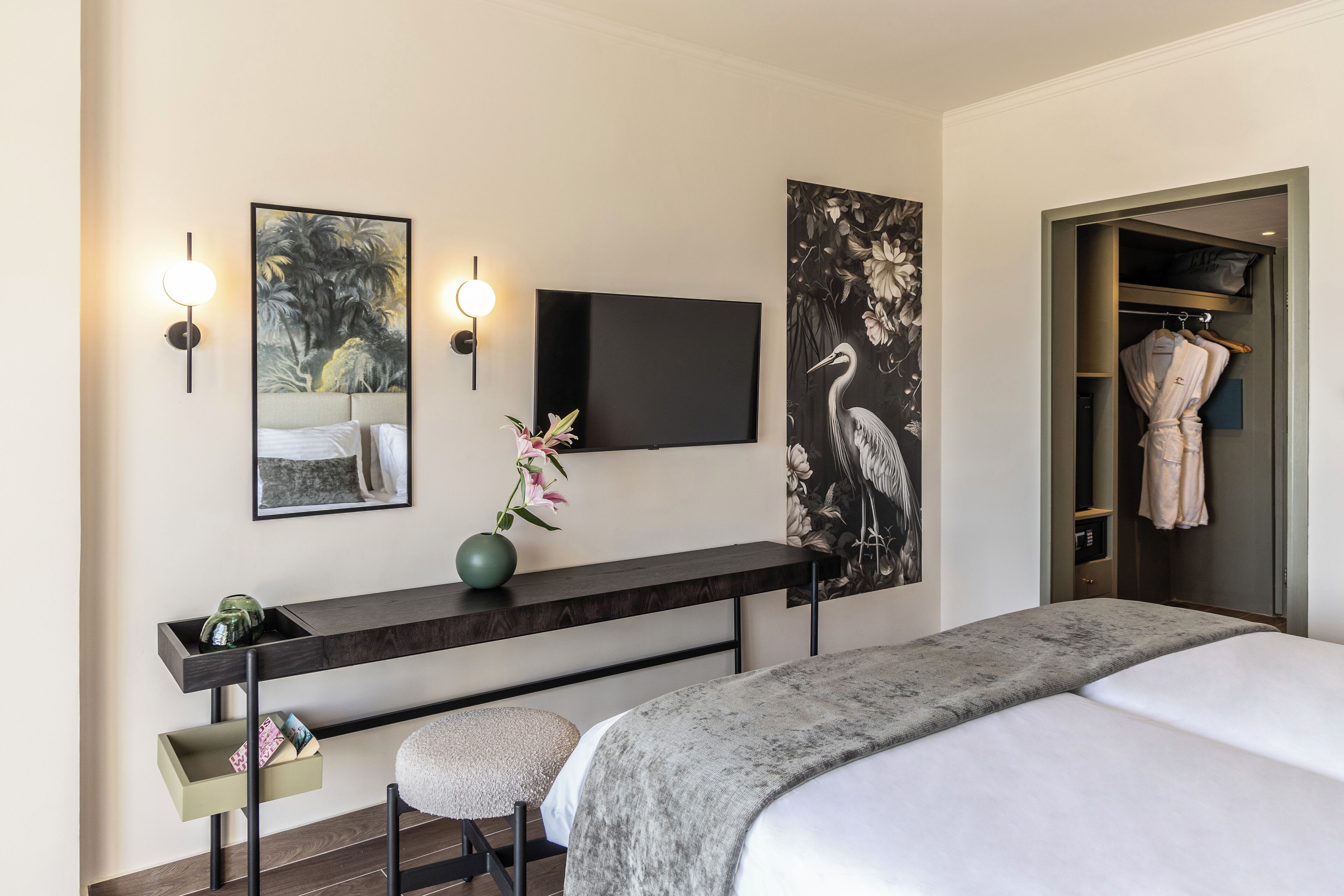 Una camera d'albergo moderna con un letto, una scrivania con televisore a schermo piatto, un vaso con fiori e opere d'arte alle pareti.
