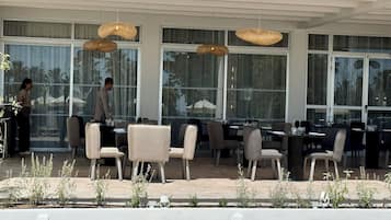 Un espace de restauration en plein air doté de nombreuses tables et chaises, de grandes fenêtres et de lampes en osier suspendues.