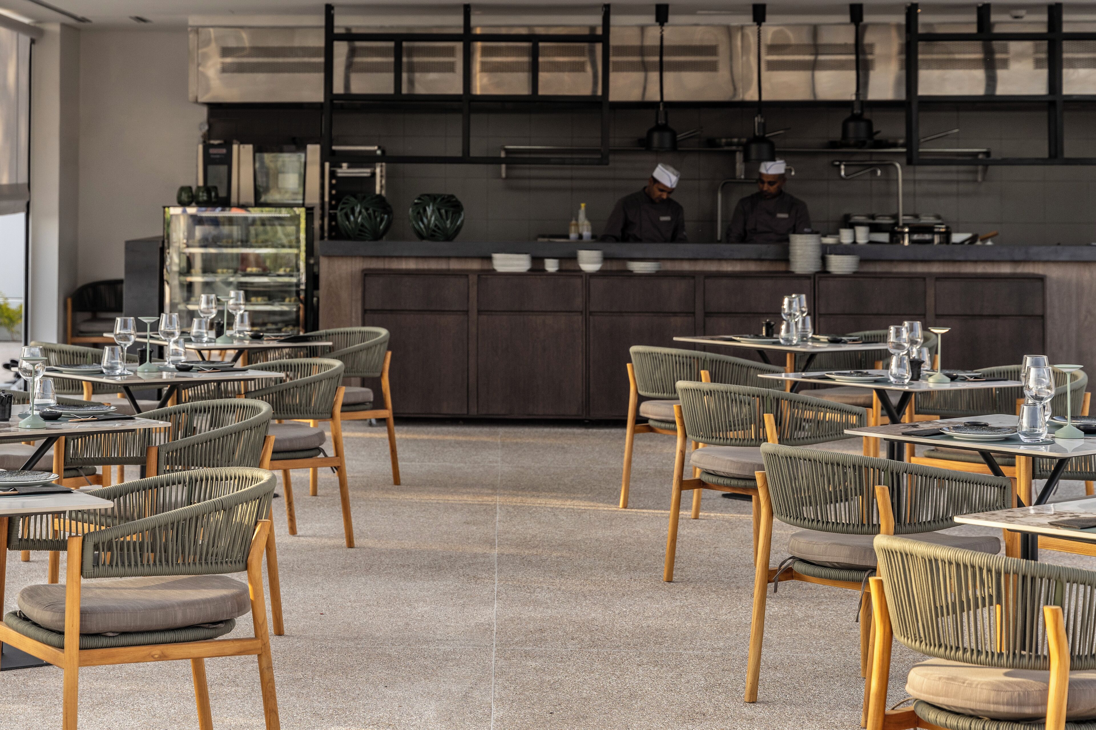 A restaurant with outdoor seating, a chef preparing food, and a dessert display.
