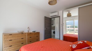 A bedroom with a bed, a wooden dresser, a wardrobe, and a view of a balcony.