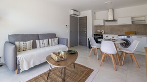 A modern living room with a grey sofa, a coffee table, and a dining area with white chairs.