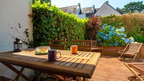 A wooden deck with a table and chairs, surrounded by lush greenery and a wooden fence. - Les Cormorans - Appt en rdc avec jardin (Benodet)