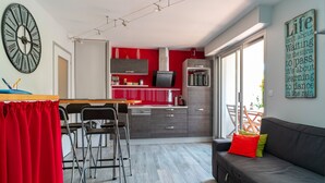 A modern kitchen with red cabinets, a large clock, and a dining area with a red curtain. - Les Cormorans - Appt en rdc avec jardin (Benodet)