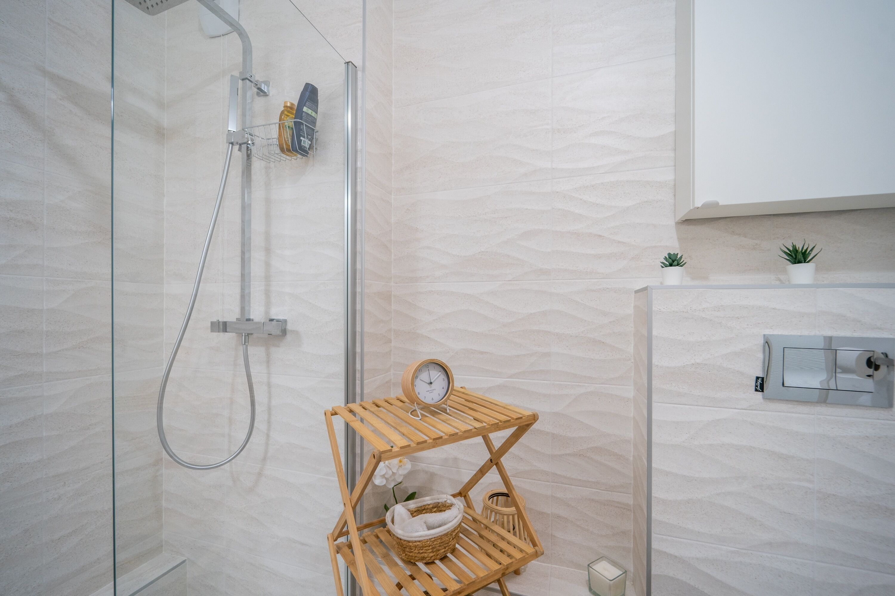 Une salle de bain moderne avec une douche à parois de verre, une étagère en bois avec une horloge et une petite plante en pot.