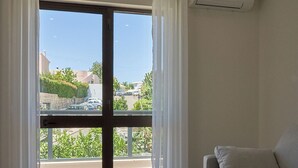 A room with a sliding glass door leading to a balcony, a beige sofa, and an air conditioning unit on the wall. - LEGACY SUITES & APARTMENTS ALBUFEIRA AL (Albufeira)